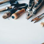 Assortment of essential DIY home repair tools neatly arranged on a wooden surface, including a hammer, screwdriver set, adjustable wrench, pliers, utility knife, tape measure, level, power drill with various bits, stud finder, and a compact ladder, symbolizing a well-equipped toolbox for home maintenance and DIY projects.